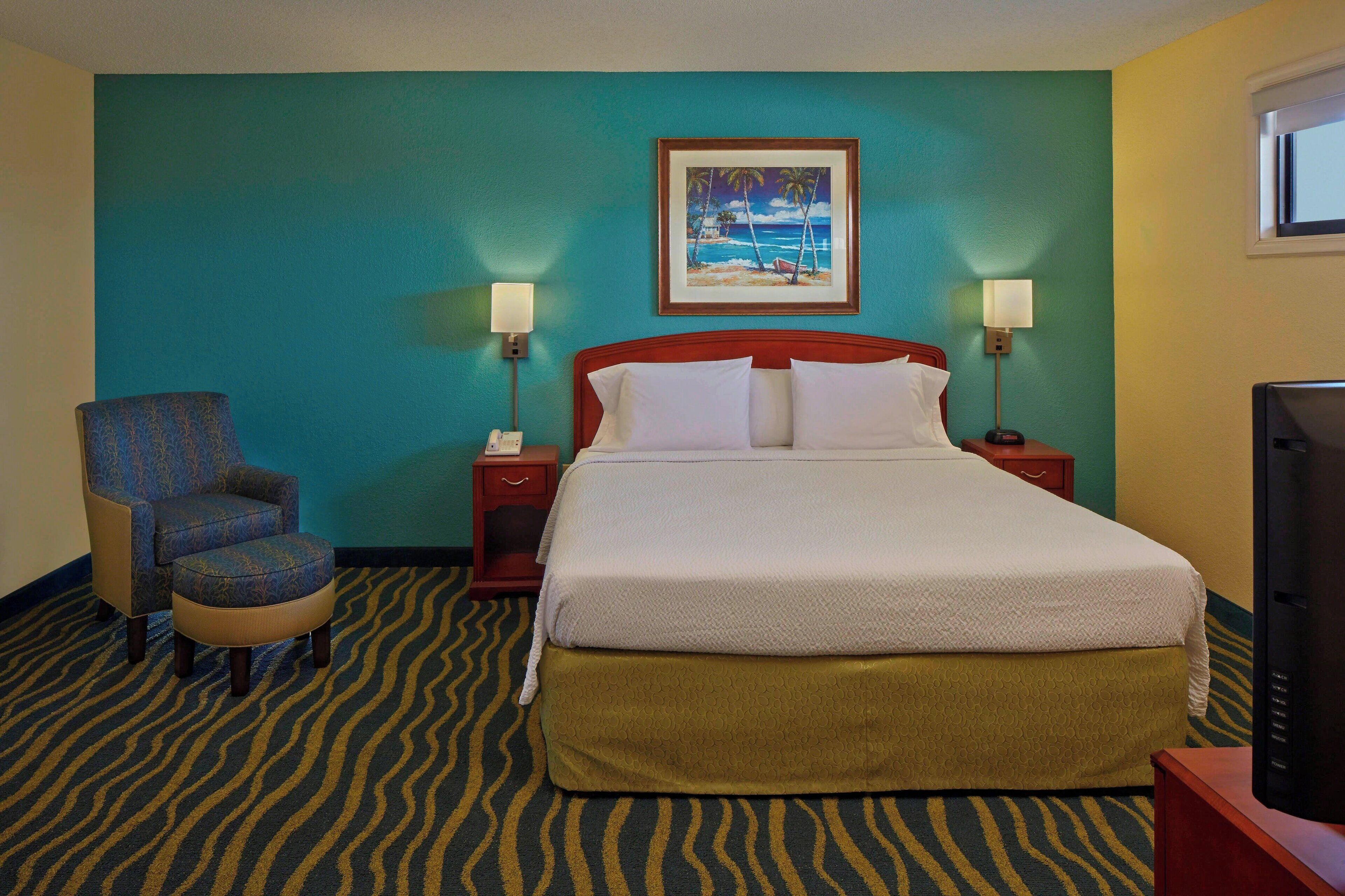 A hotel room with a bed, a chair, a nightstand, a lamp, and a television.