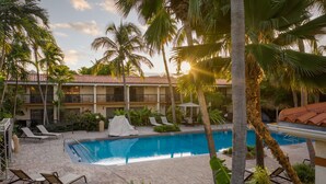 A pool area with lounge chairs, palm trees, and a building with a tiled roof. - Courtyard by Marriott Key West Waterfront (Key West)