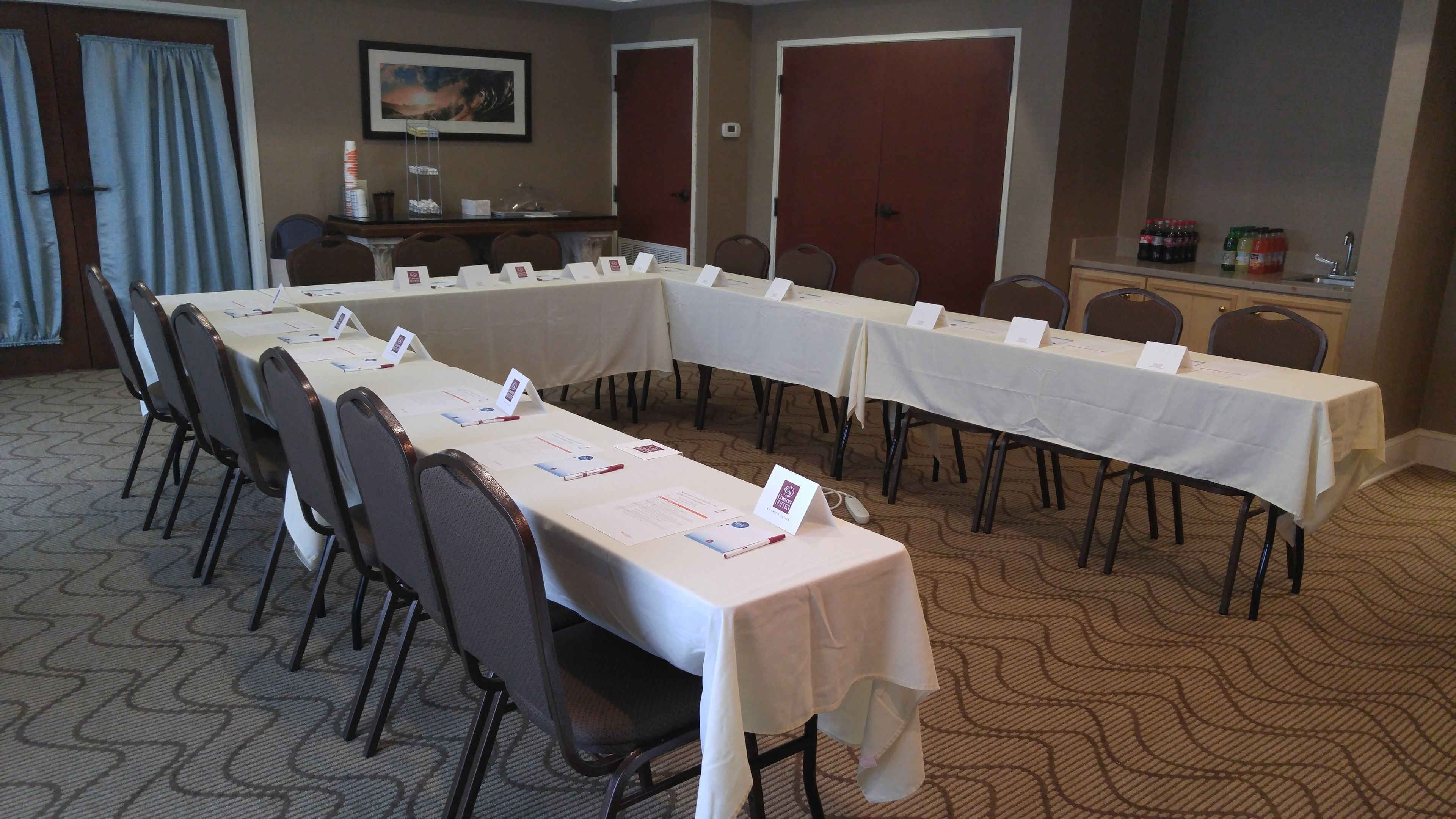 A conference room with long tables, chairs, nameplates, and a buffet area with beverages.