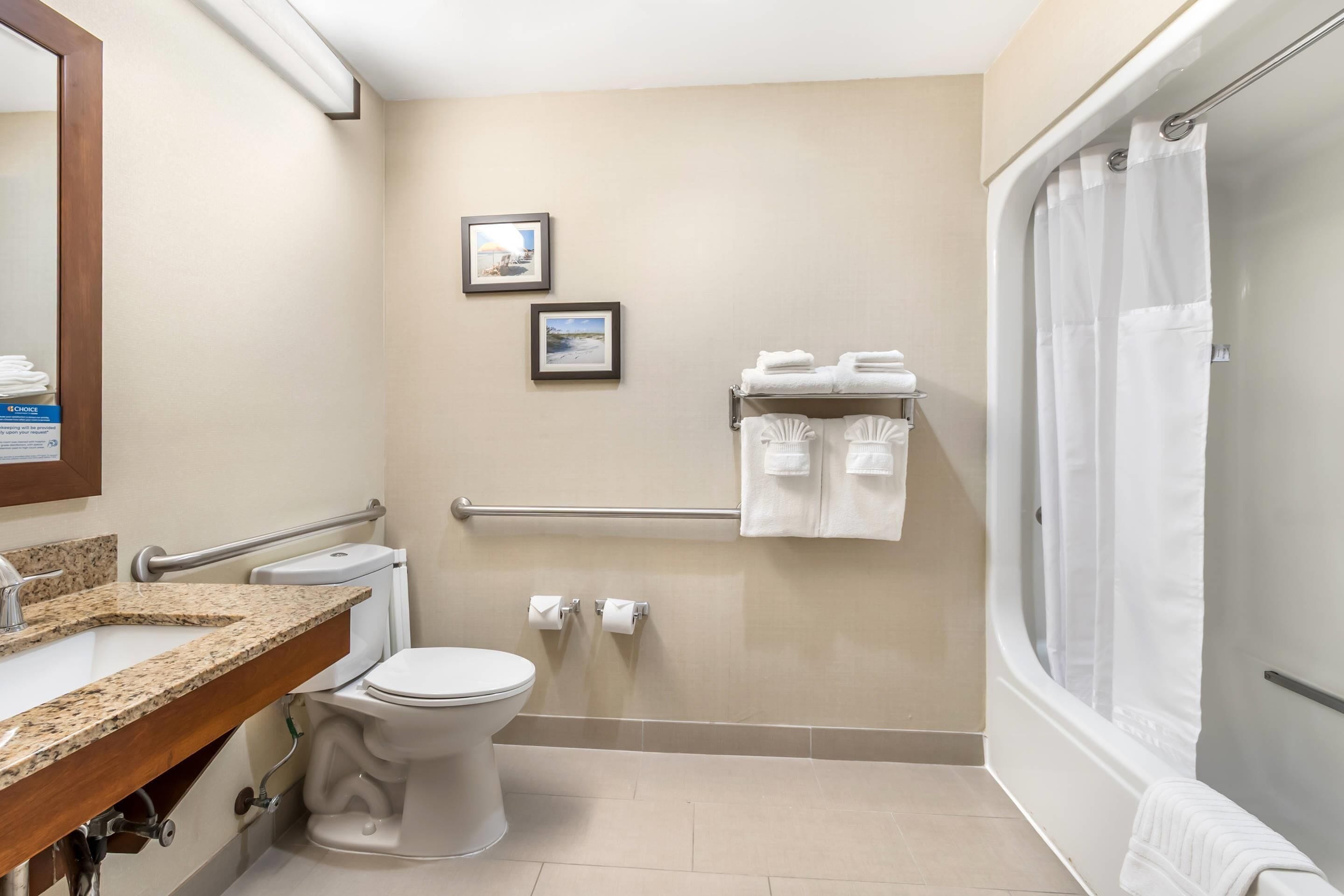 A bathroom with a toilet, sink, and shower. There are towels and a framed picture on the wall.