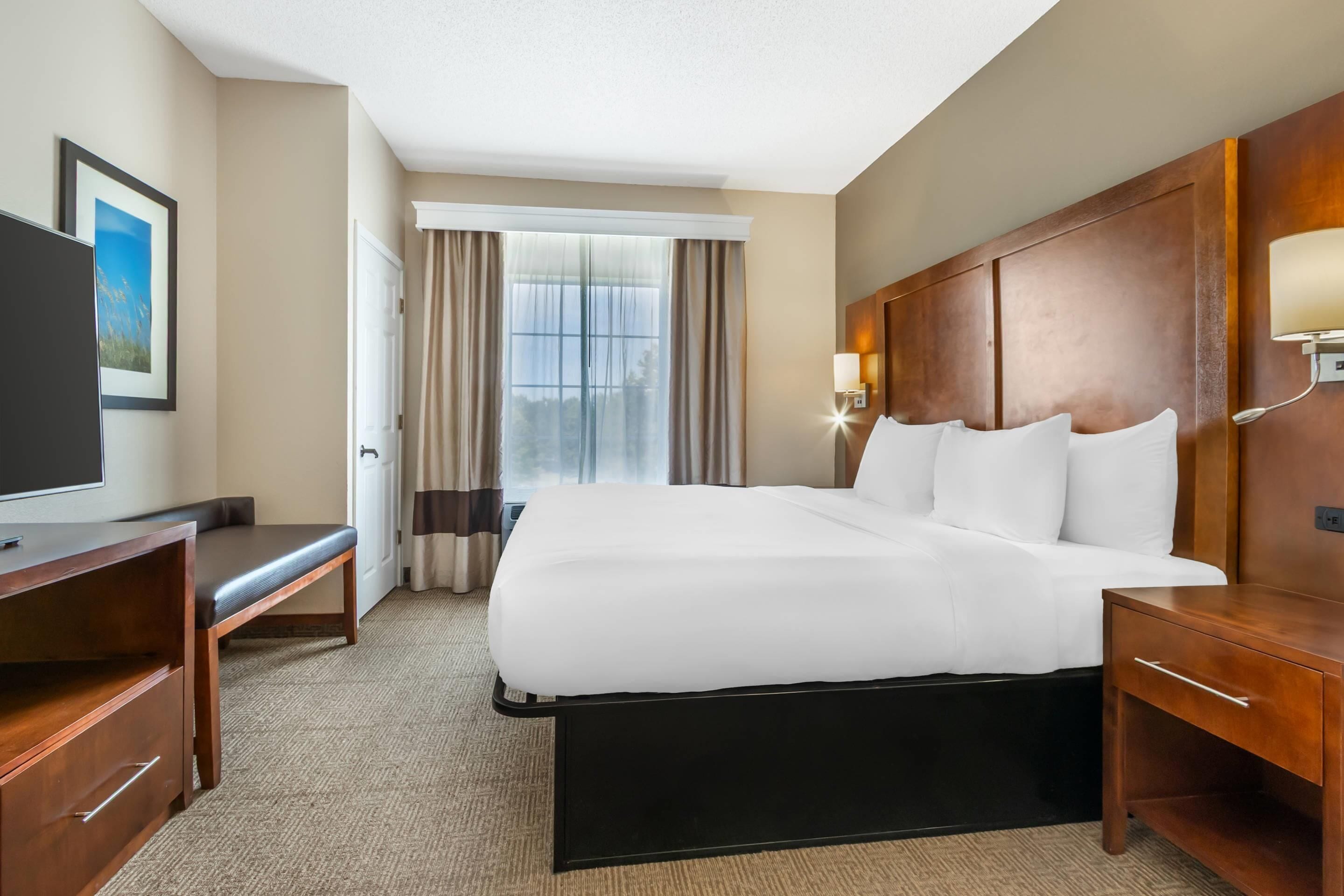 A hotel room with a large bed, a desk with a chair, a TV, and a window with curtains.