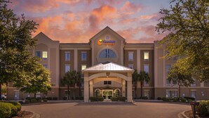 A Comfort Suites hotel with a central entrance, surrounded by palm trees and a landscaped area. - Comfort Suites Myrtle Beach Central (Myrtle Beach)