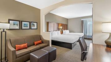 A hotel room with a bed, a sofa, a desk, and a chair. There are framed pictures on the wall.
