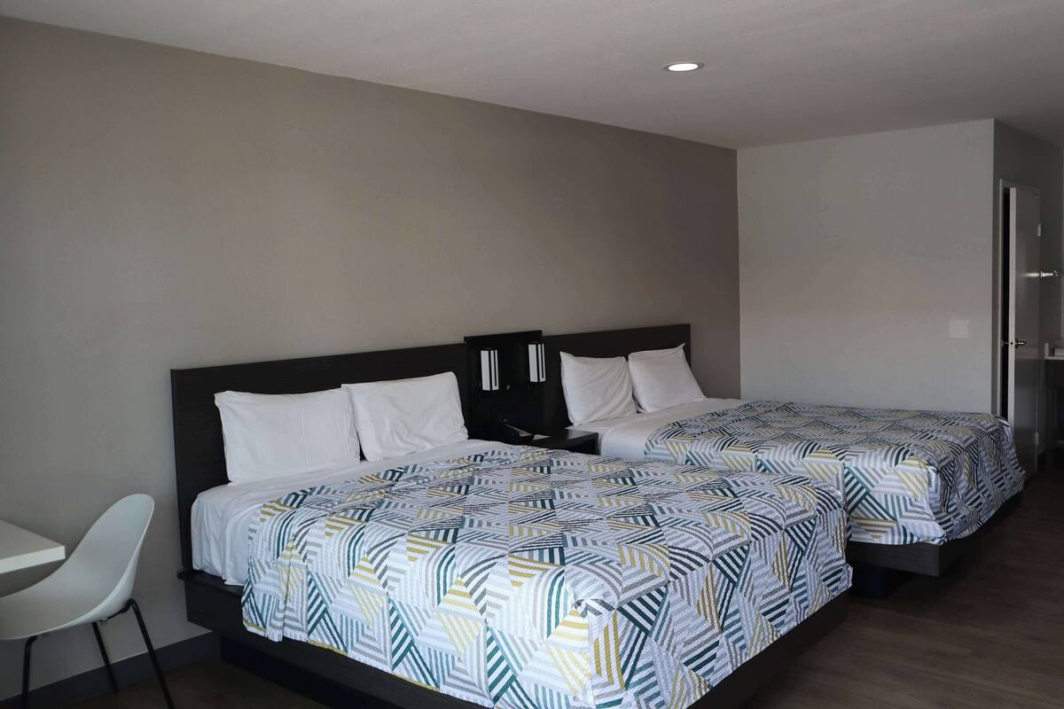 A hotel room with two beds, a desk, and a chair.