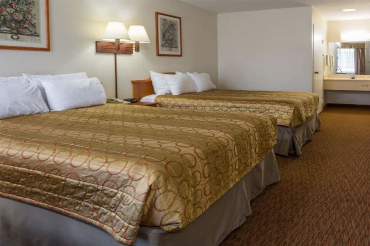 A hotel room with two beds, each with a patterned bedspread, a bedside table with a lamp, and a framed picture on the wall.
