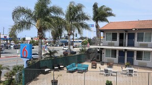 Un motel con mesas al aire libre, palmeras y un letrero de una estación de servicio Chevron cercana.