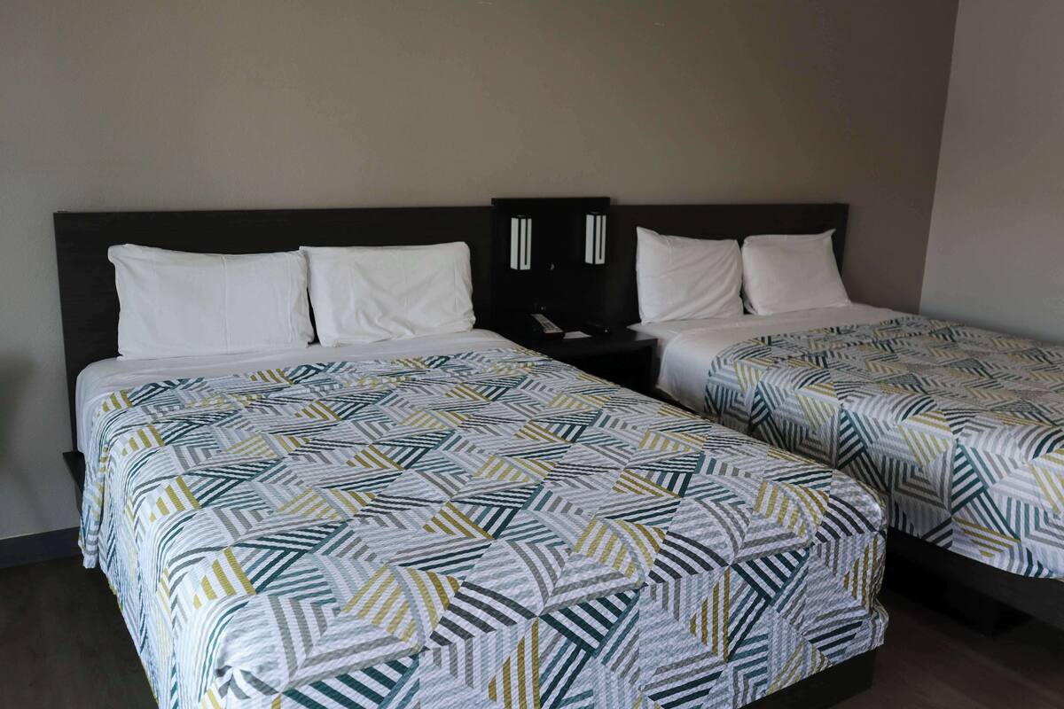 A hotel room with two single beds, each with a patterned bedspread and white pillows.