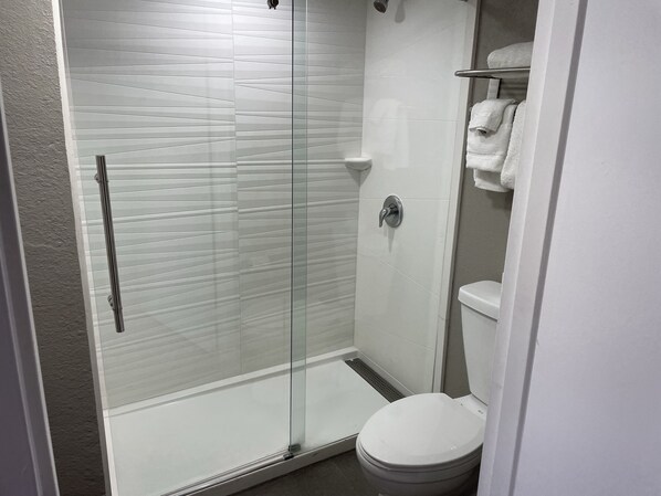 Une salle de bain moderne avec une douche à parois de verre, des toilettes blanches et un porte-serviettes.