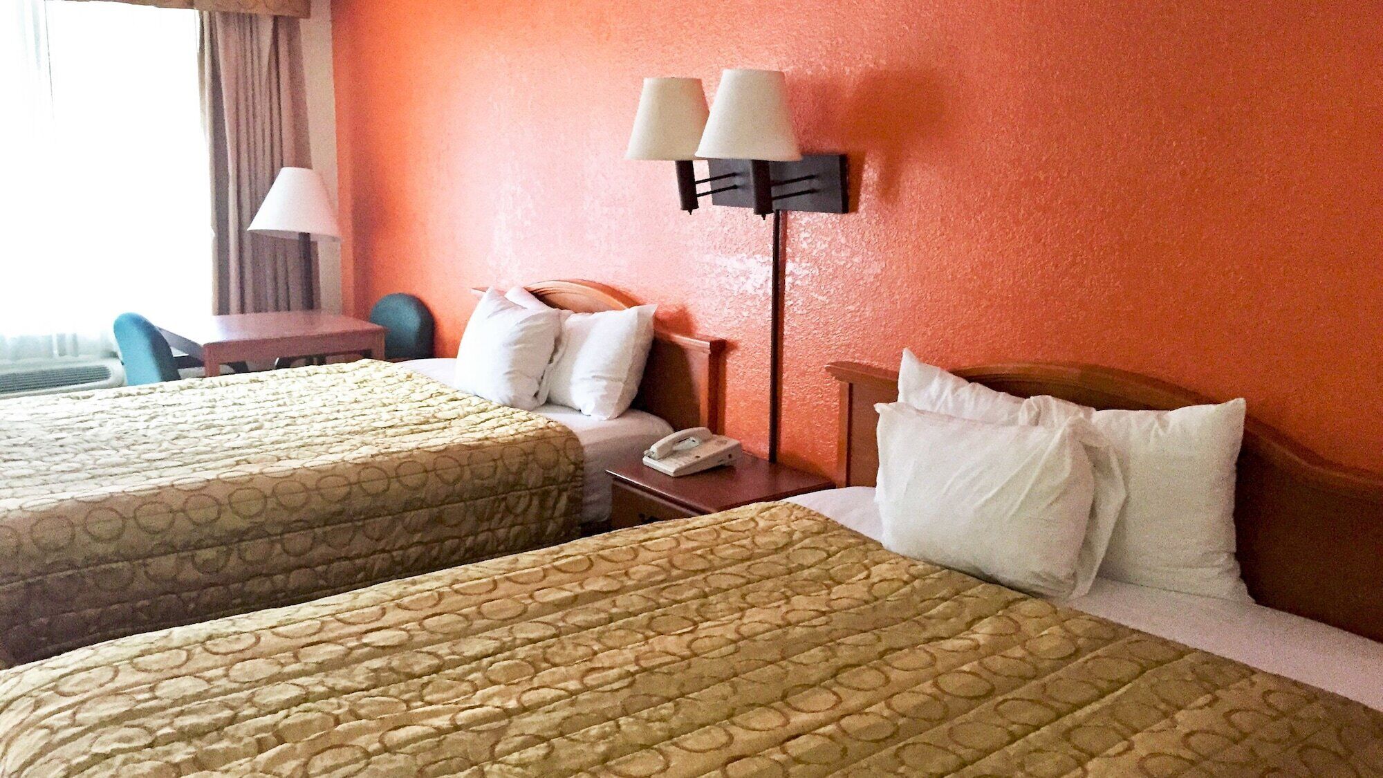 A hotel room with two beds, a desk, a chair, and a lamp.