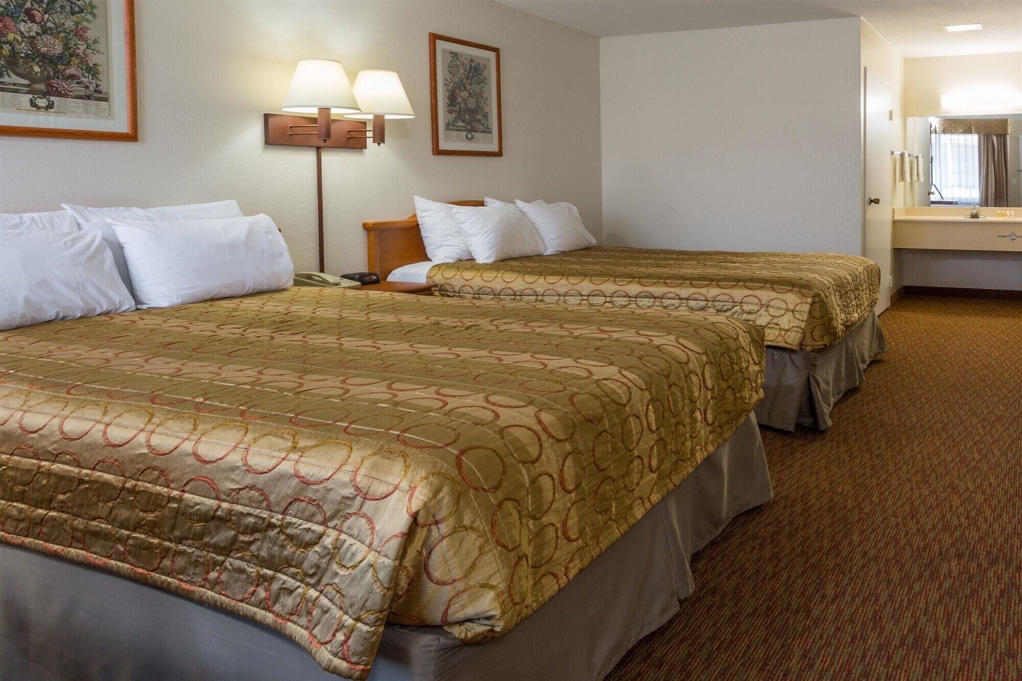 A hotel room with two beds, a bedside table, a lamp, and a mirror.