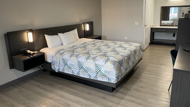 Una habitación de hotel moderna con una cama grande, mesitas de noche, un escritorio y un espejo.