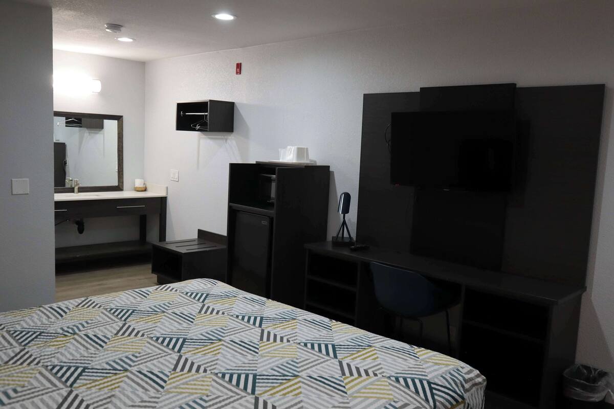 A hotel room with a bed, a desk, a chair, a TV, and a mirror.