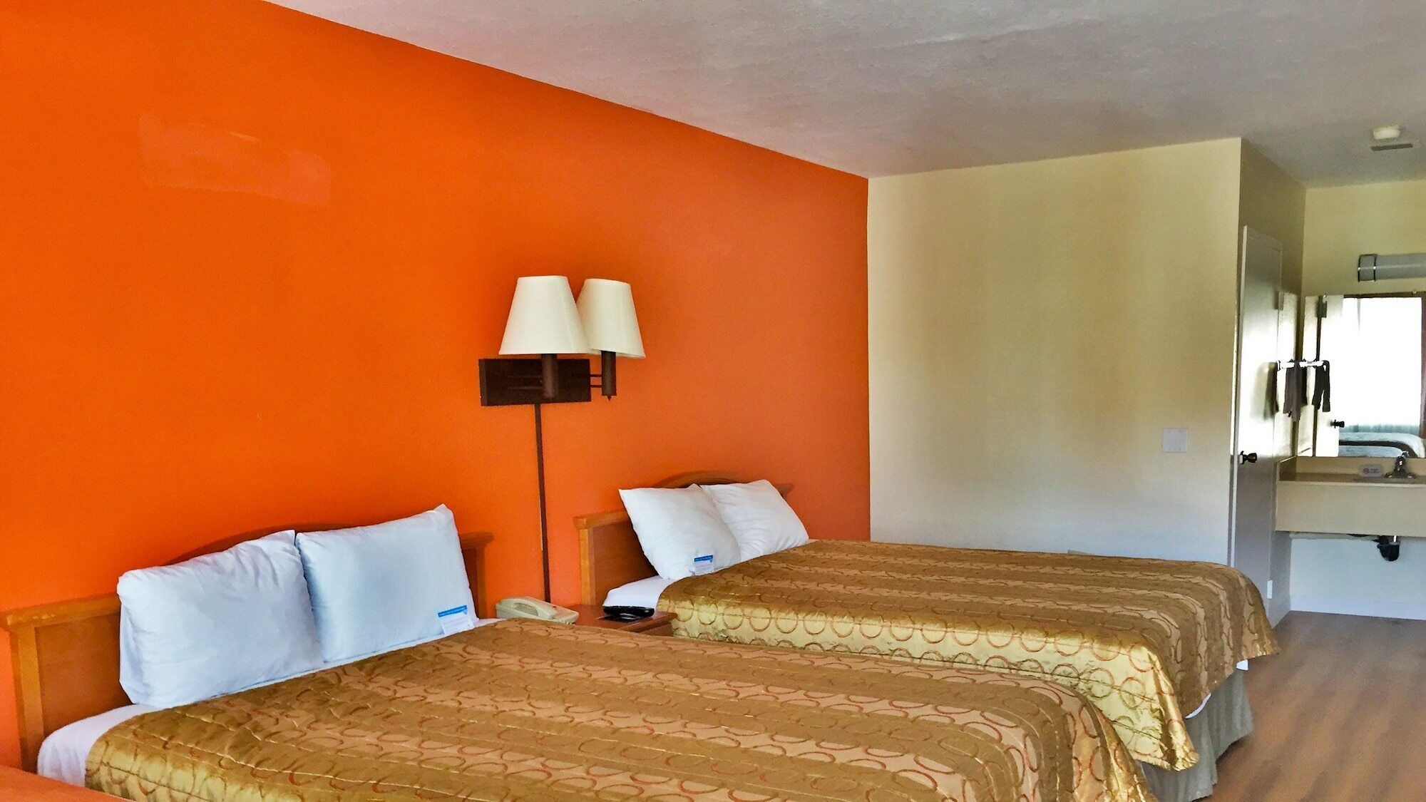 Een hotelkamer met twee bedden, een nachtkastje, een lamp en een badkamer die door een geopende deur zichtbaar is.