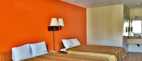 Een hotelkamer met twee bedden, een nachtkastje, een lamp en een badkamer die door een geopende deur zichtbaar is.