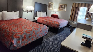 Quarto de hotel com duas camas, uma escrivaninha, uma cadeira, um abajur, um aquecedor e uma janela com cortinas.