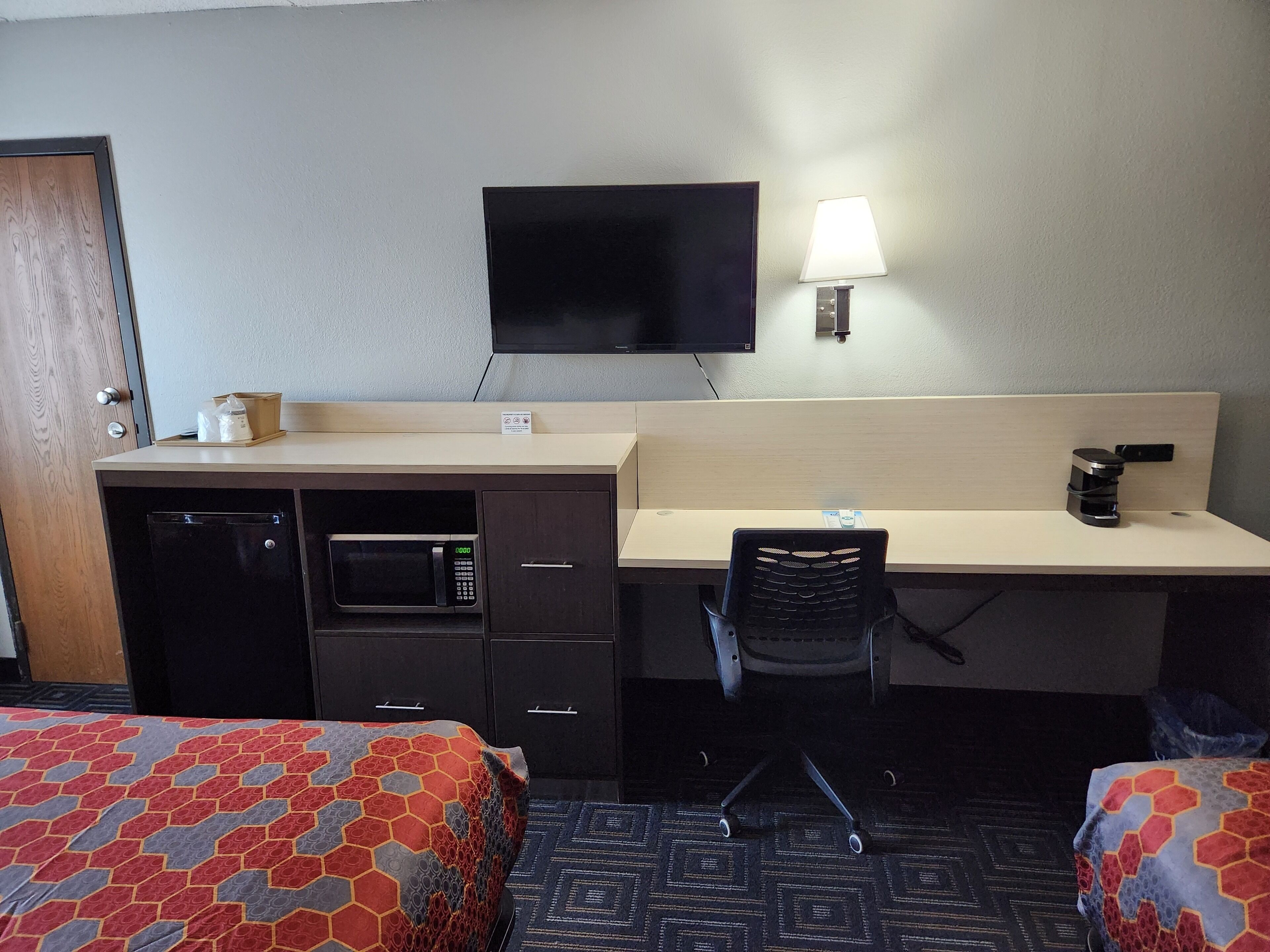 Habitación de hotel con cama, escritorio con silla, microondas, cafetera y televisión.