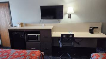 Habitación de hotel con cama, escritorio con silla, microondas, cafetera y televisión.