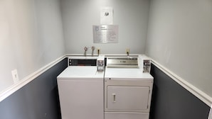 Uma lavanderia com duas máquinas de lavar e uma secadora, uma placa com regras de lavanderia e uma tomada na parede.