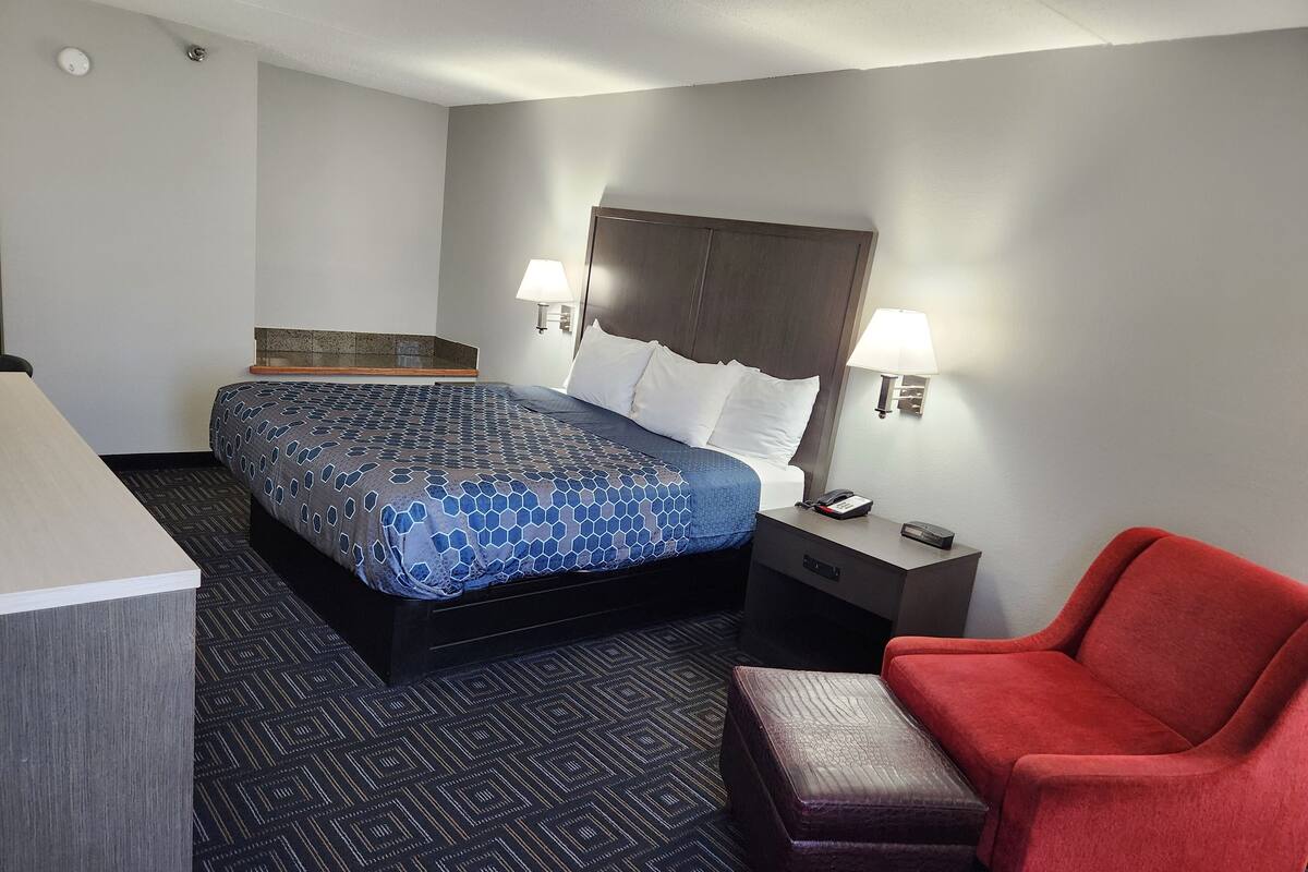 Une chambre d’hôtel avec un lit, une table de chevet, une lampe et une chaise rouge.