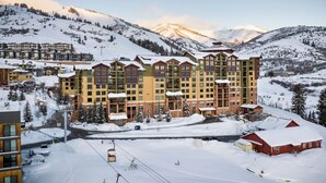 A multi-story hotel with a ski lift in the foreground, surrounded by snow-covered mountains. - Grand Summit Hotel - Canyons Village, a RockResort (Park City)