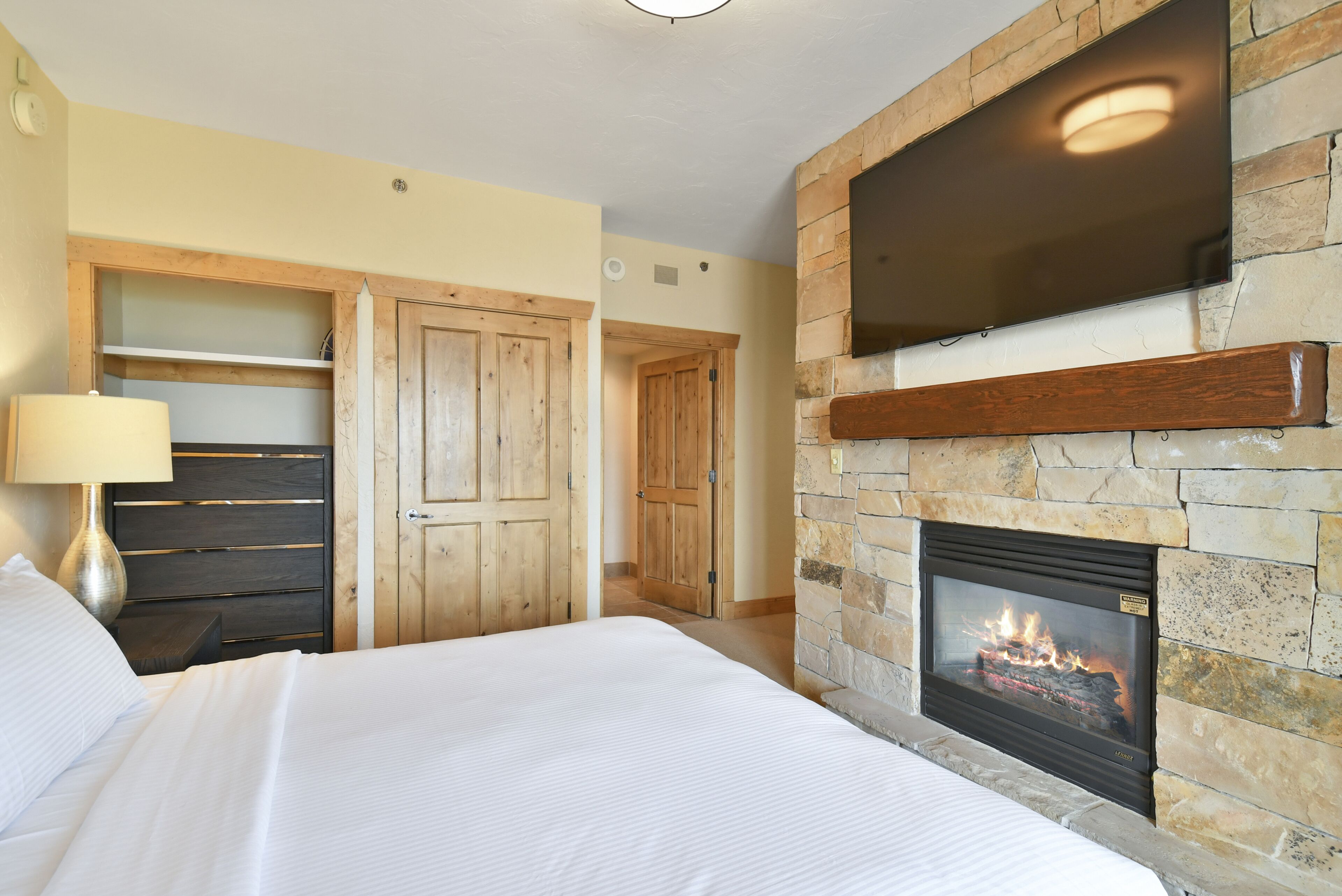 A bedroom with a stone fireplace, wooden wardrobe, and a TV mounted on the wall.