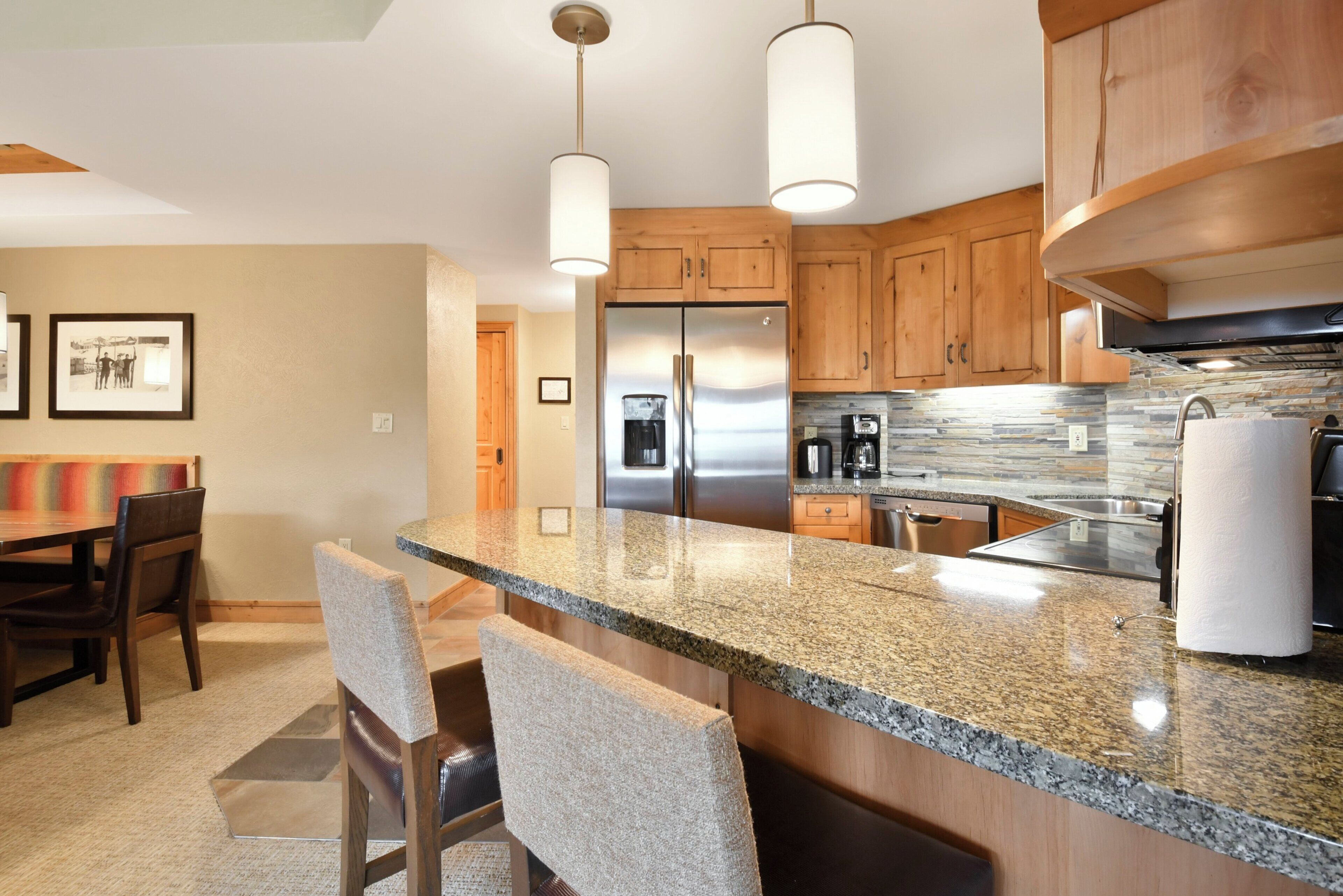A modern kitchen with granite countertops, stainless steel appliances, wooden cabinets, and pendant lighting.