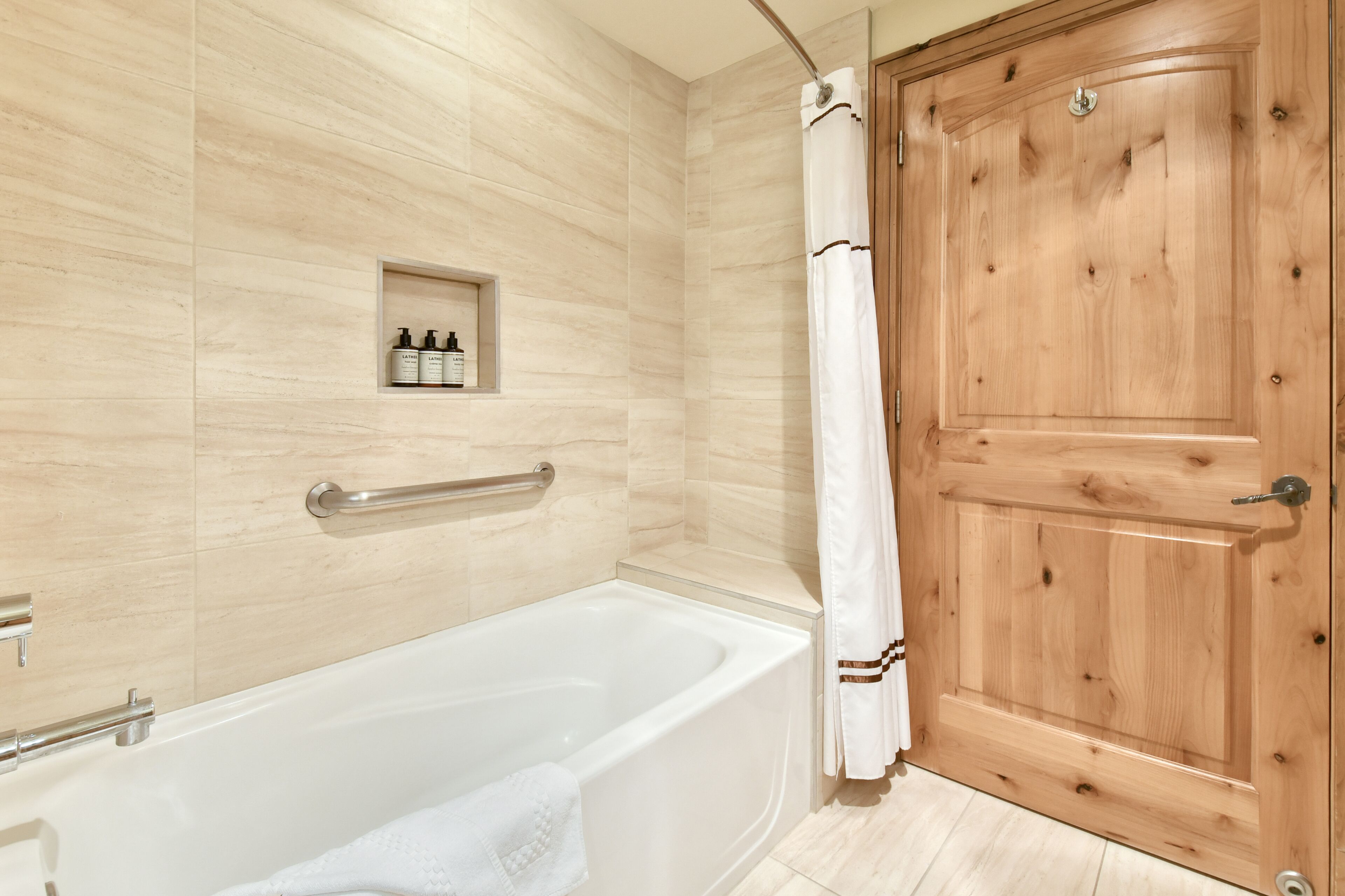 A bathroom with a bathtub, a wooden door, and a shelf with toiletries.