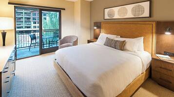 A hotel room with a large bed, a desk, a chair, a balcony with a view, and artwork on the wall.