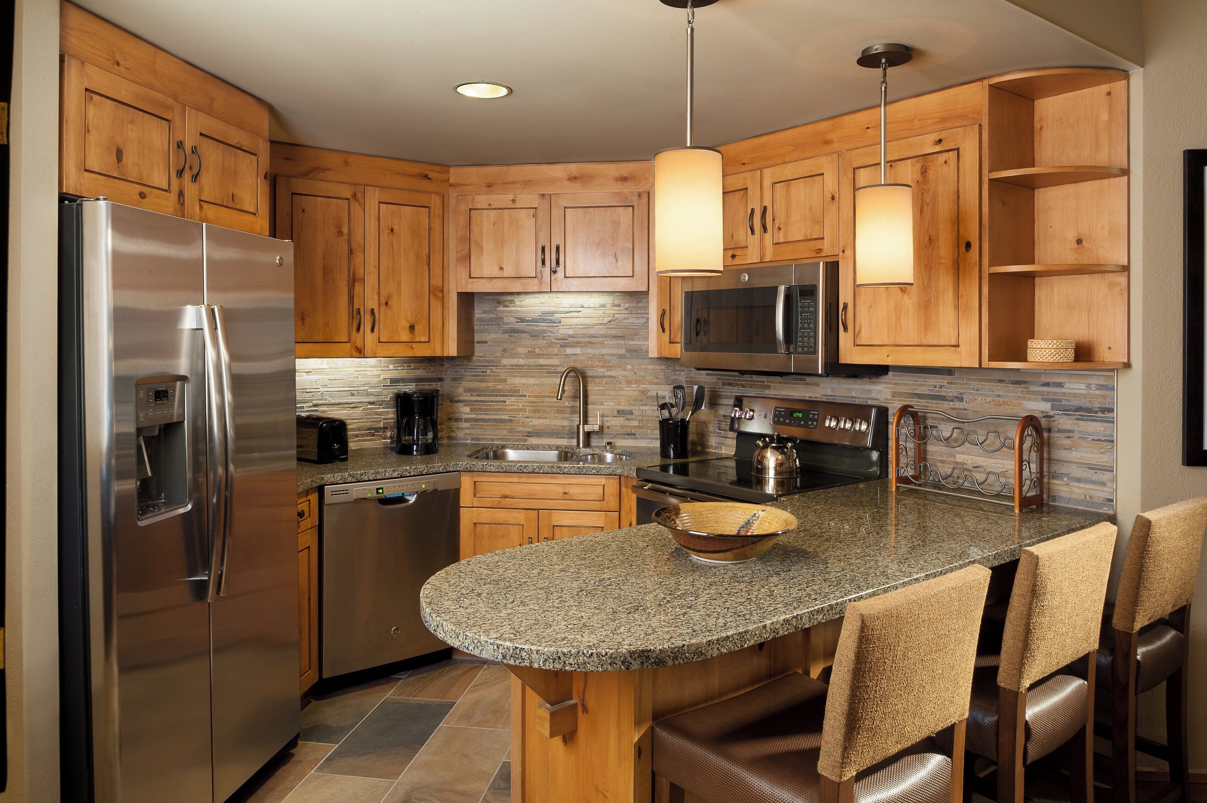 Una cocina moderna con armarios de madera, electrodomésticos de acero inoxidable, encimera de granito y una isla integrada con taburetes de bar.