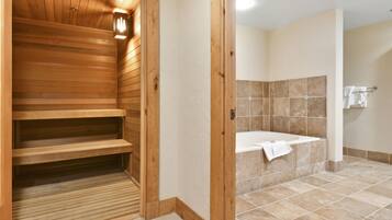 A wooden sauna with benches and a tiled shower area with a bathtub.
