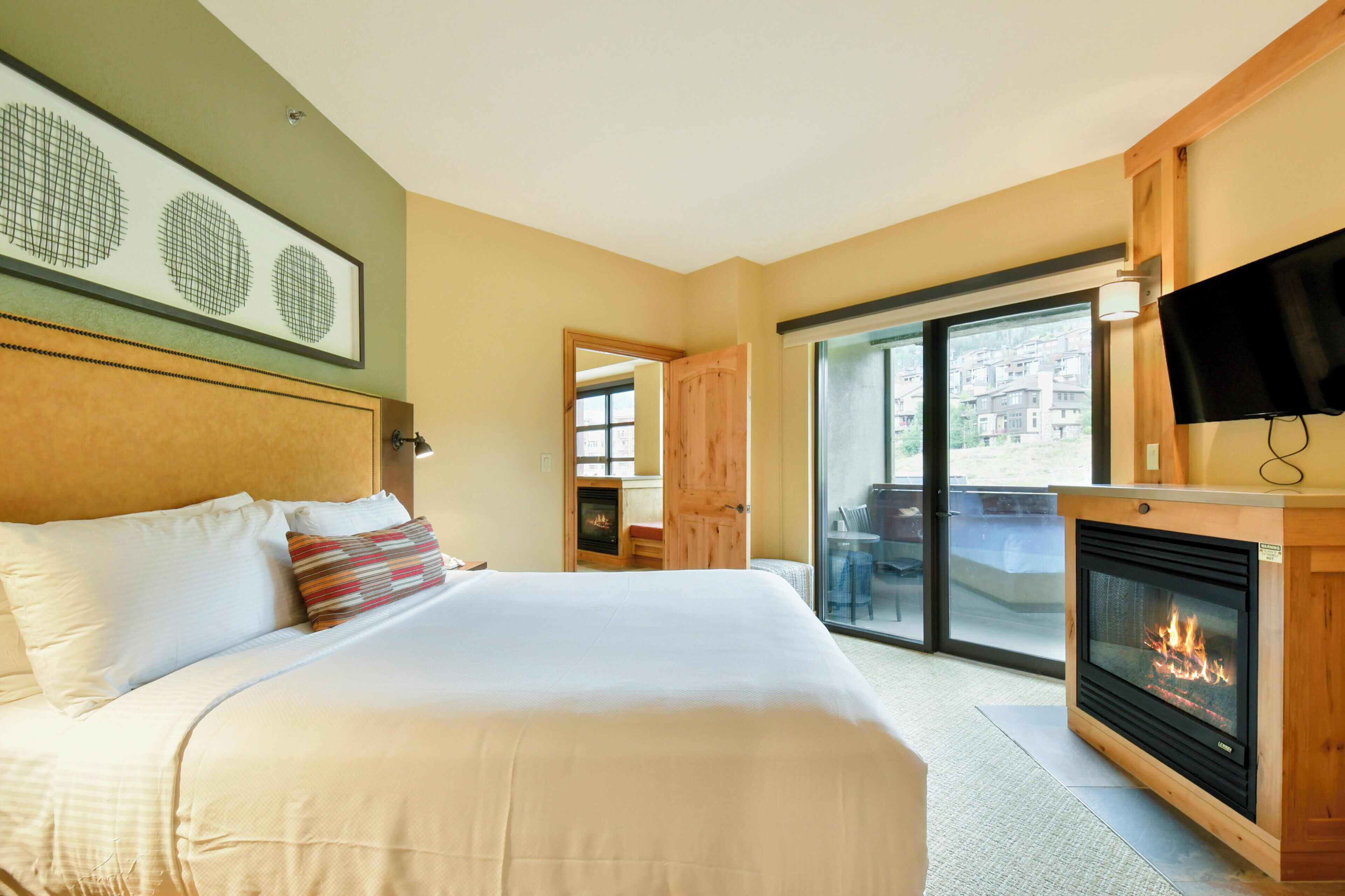 Una camera d'albergo con un letto grande, un camino, una televisione e un balcone con vista sugli edifici.