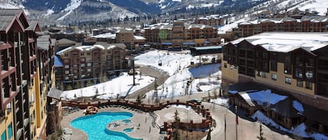 A resort with a central swimming pool, multiple buildings, and a mountainous backdrop.