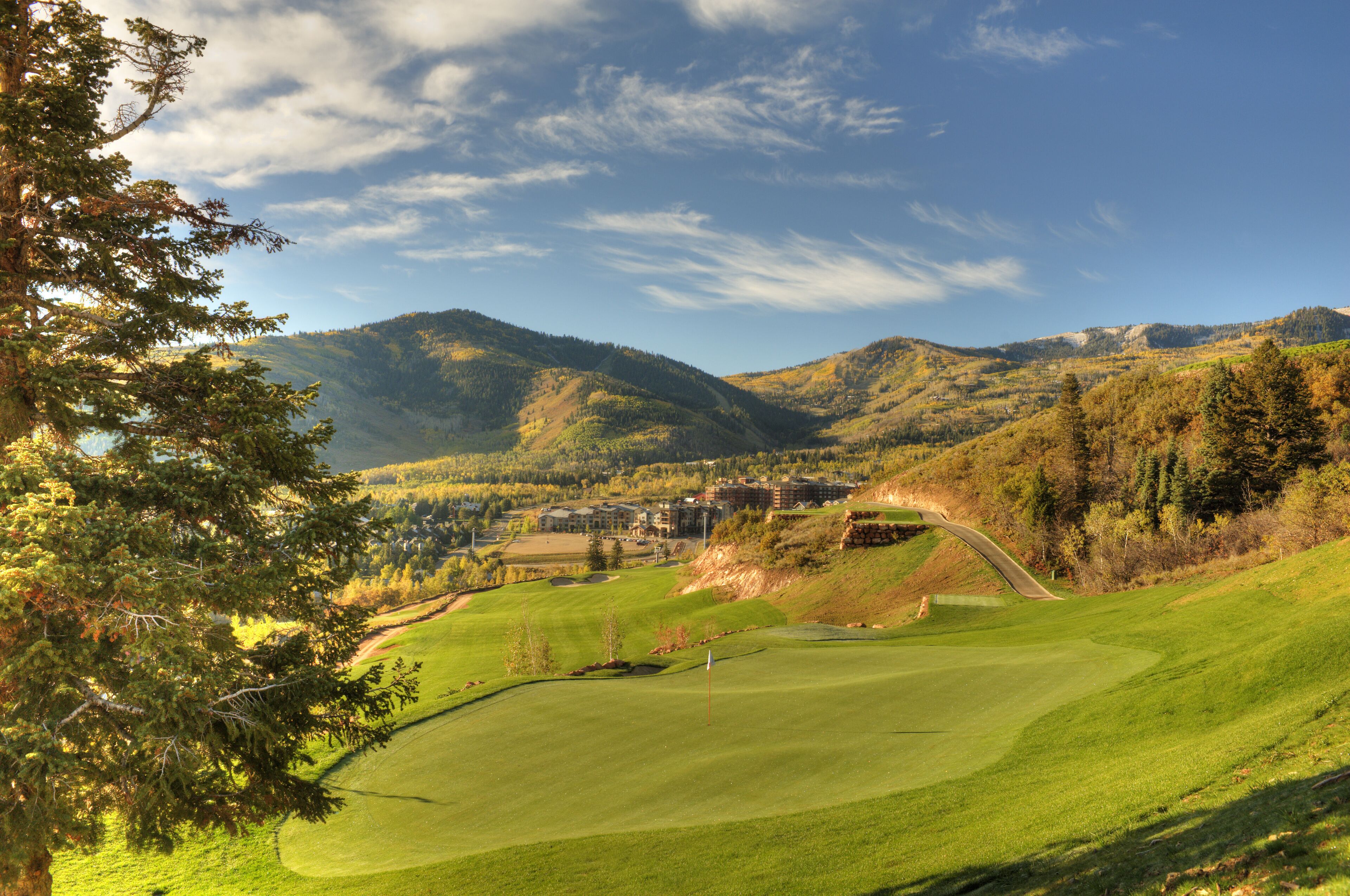 Un parcours de golf avec un mât de drapeau, entouré de montagnes et d’arbres.