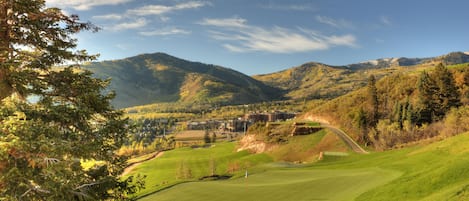 Un parcours de golf avec un mât de drapeau, entouré de montagnes et d’arbres.