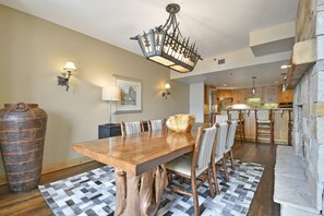 A dining area with a wooden table and chairs, a chandelier, and a stone wall. - Grand Summit Hotel - Canyons Village, a RockResort (Park City)