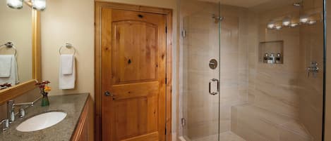 A bathroom with a wooden door, a glass-enclosed shower, and a granite countertop with a sink and mirror.