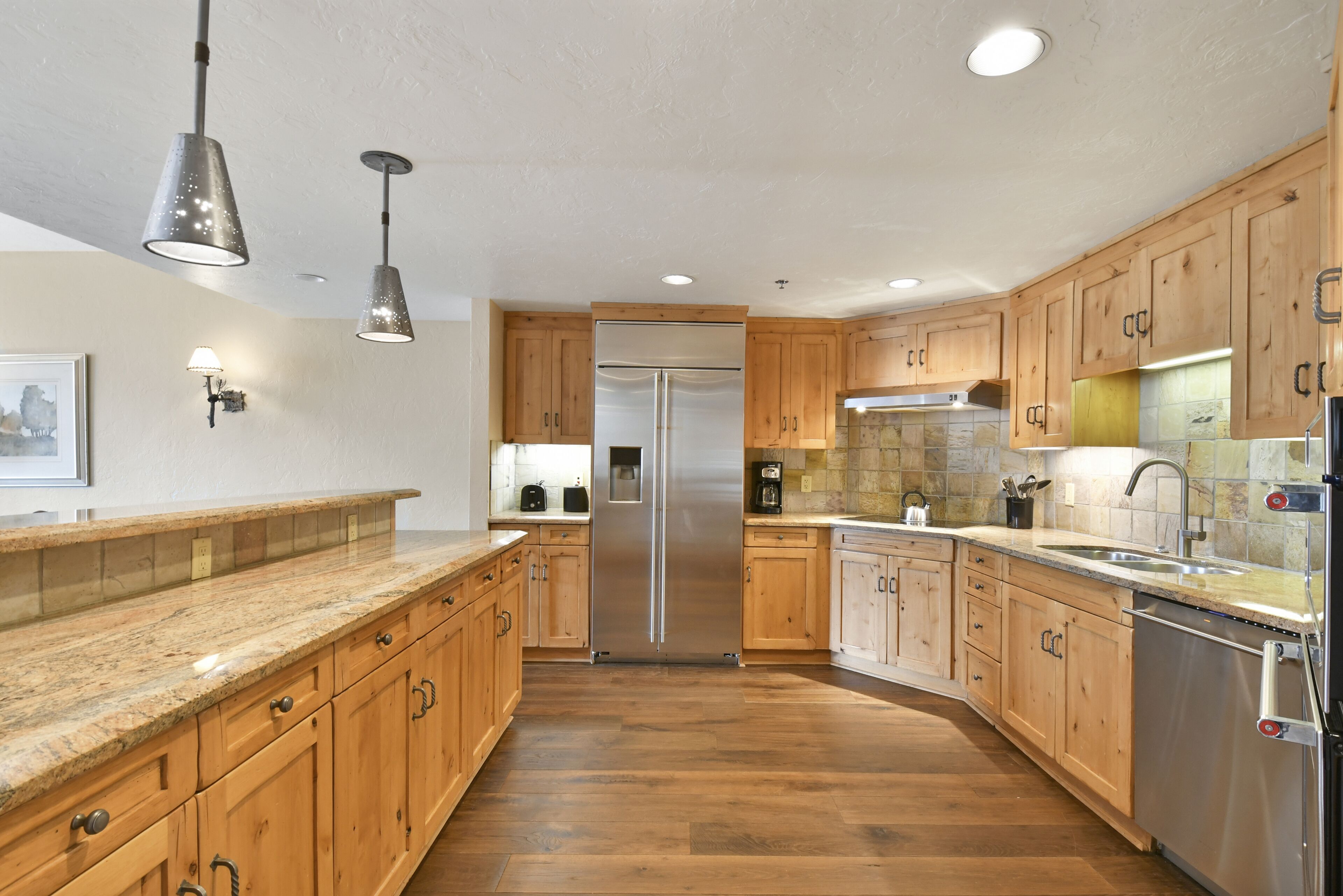 A modern kitchen with wooden cabinets, stainless steel appliances, and pendant lighting.