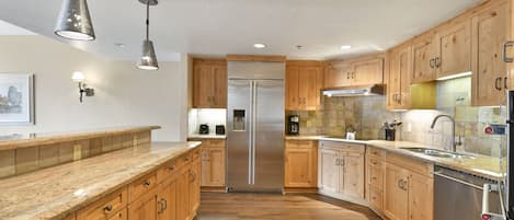 A modern kitchen with wooden cabinets, stainless steel appliances, and pendant lighting.
