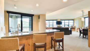 A modern kitchen with a granite countertop, wooden bar stools, and a large window overlooking a scenic view.