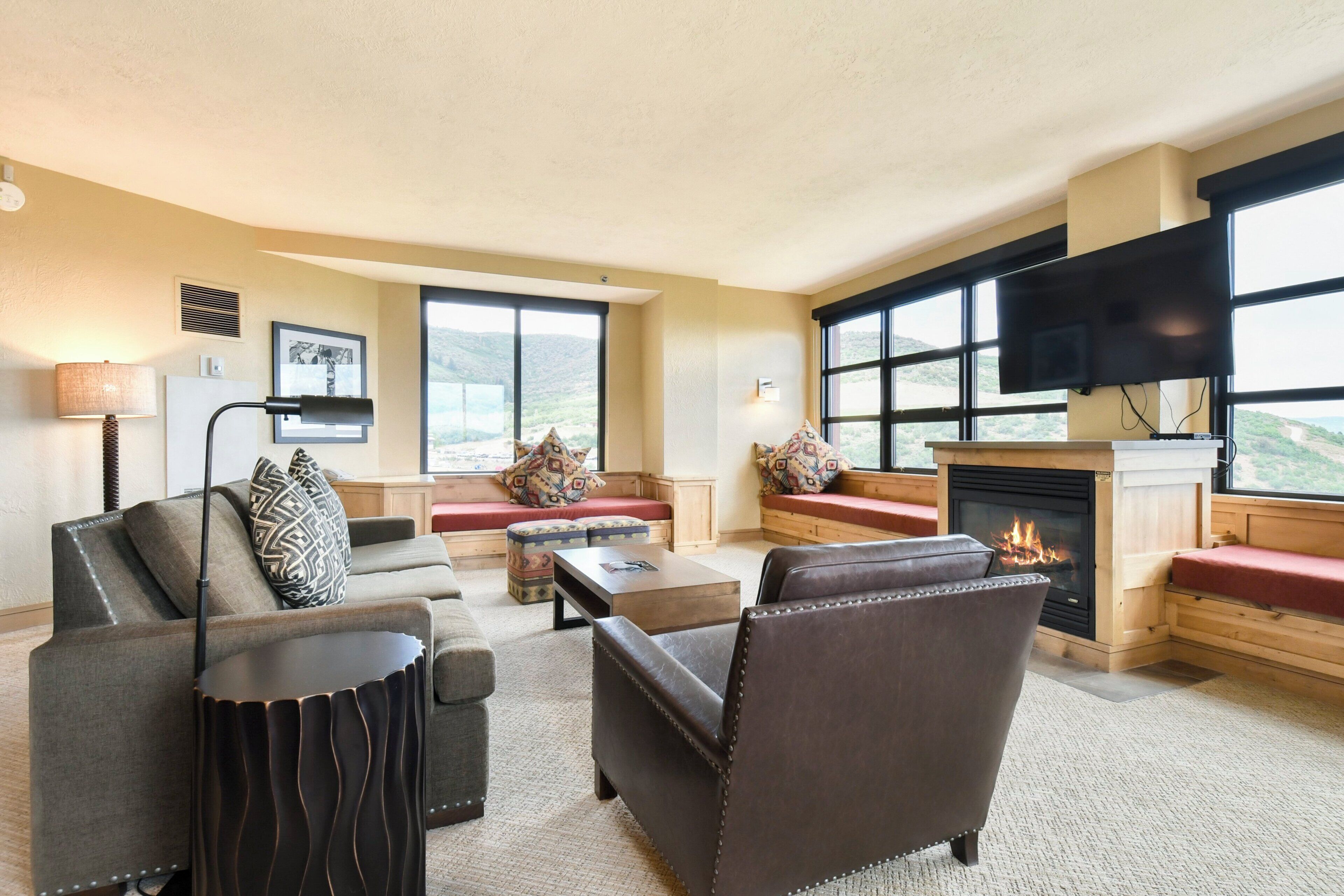 A spacious living room with a fireplace, comfortable seating, and large windows offering a view of the outdoors.