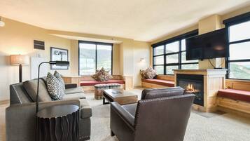 A spacious living room with a fireplace, comfortable seating, and large windows offering a view of the outdoors.