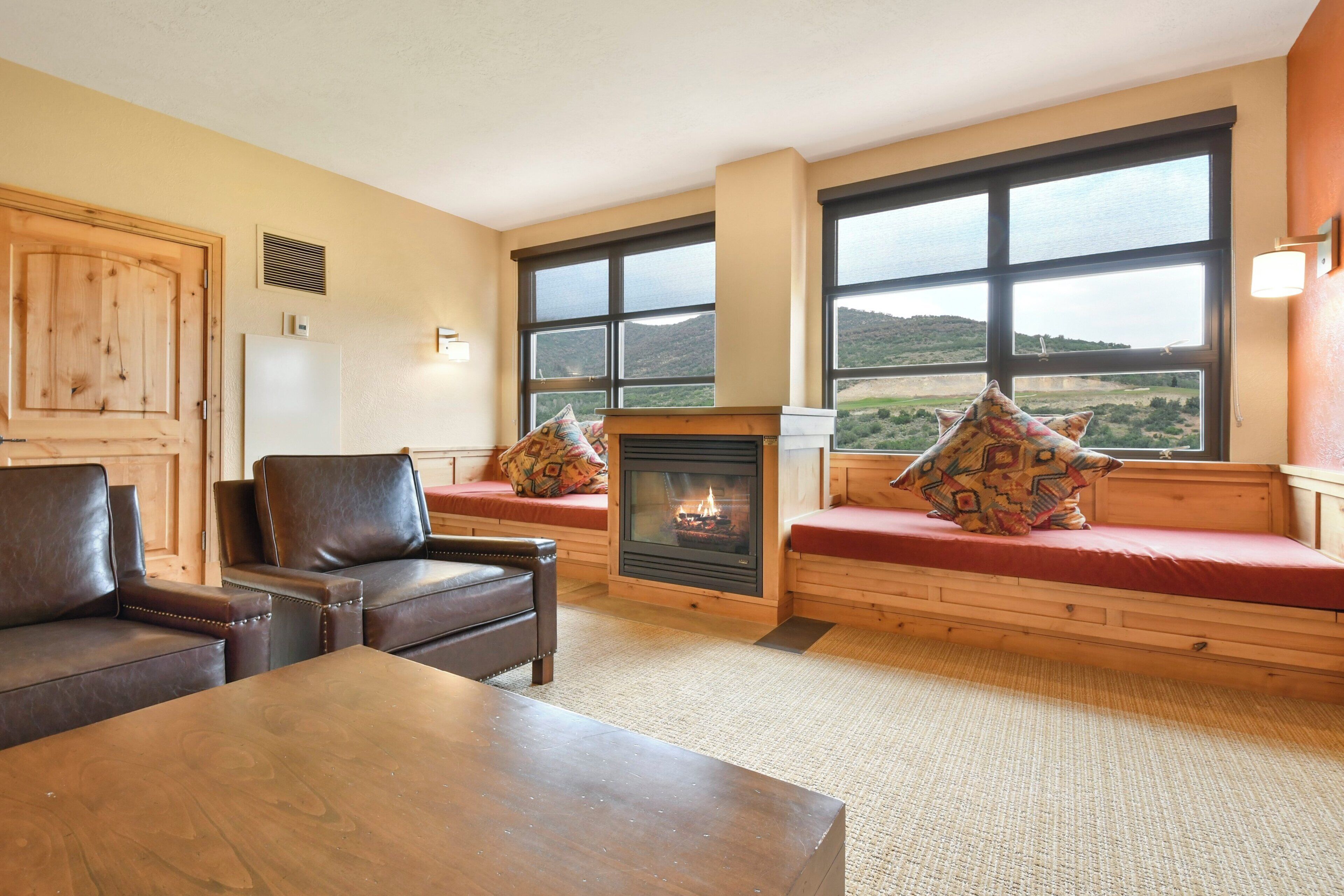 A cozy living room with a fireplace, leather sofas, and large windows offering a view of the countryside.