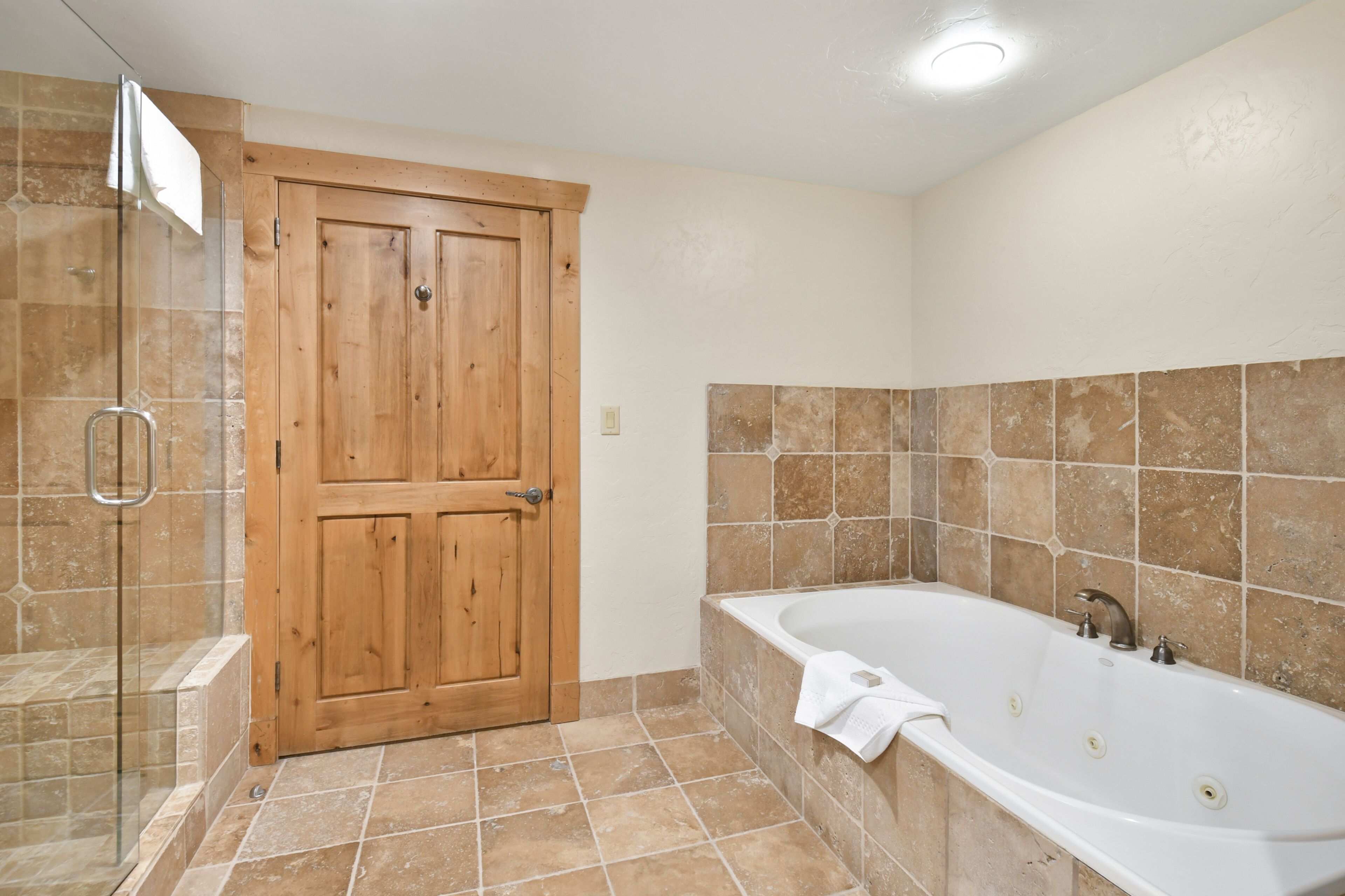A bathroom with a wooden door, a glass shower enclosure, and a bathtub with a towel.