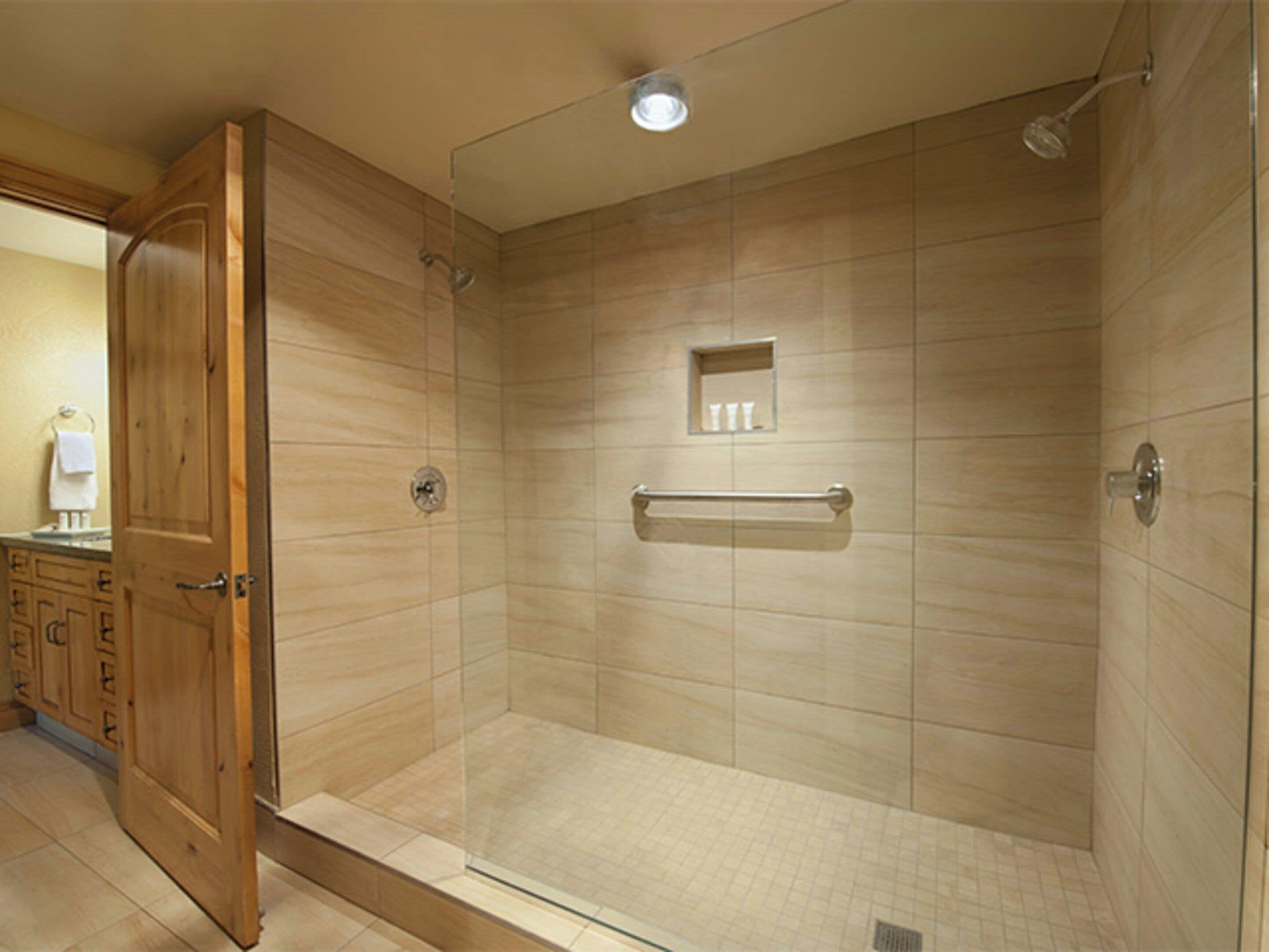 A walk-in shower with a glass door, beige tiled walls, a small shelf with toiletries, and a towel rack.