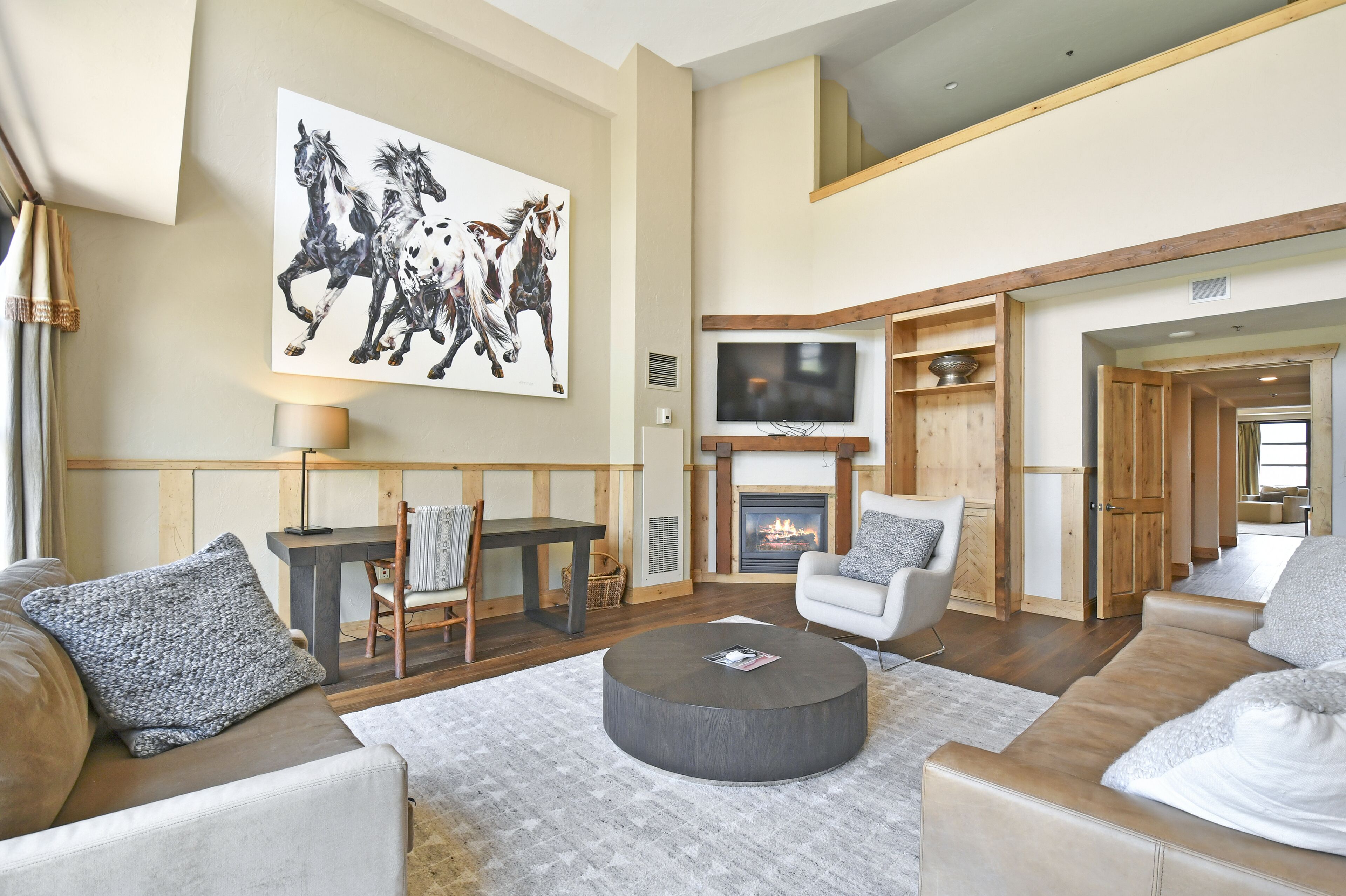 A spacious living room with a fireplace, a television, and a large horse painting on the wall.