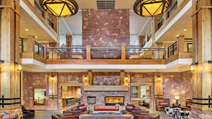 A spacious lobby with a stone fireplace, wooden furniture, and a second-floor balcony with a railing. - Grand Summit Hotel - Canyons Village, a RockResort (Park City)