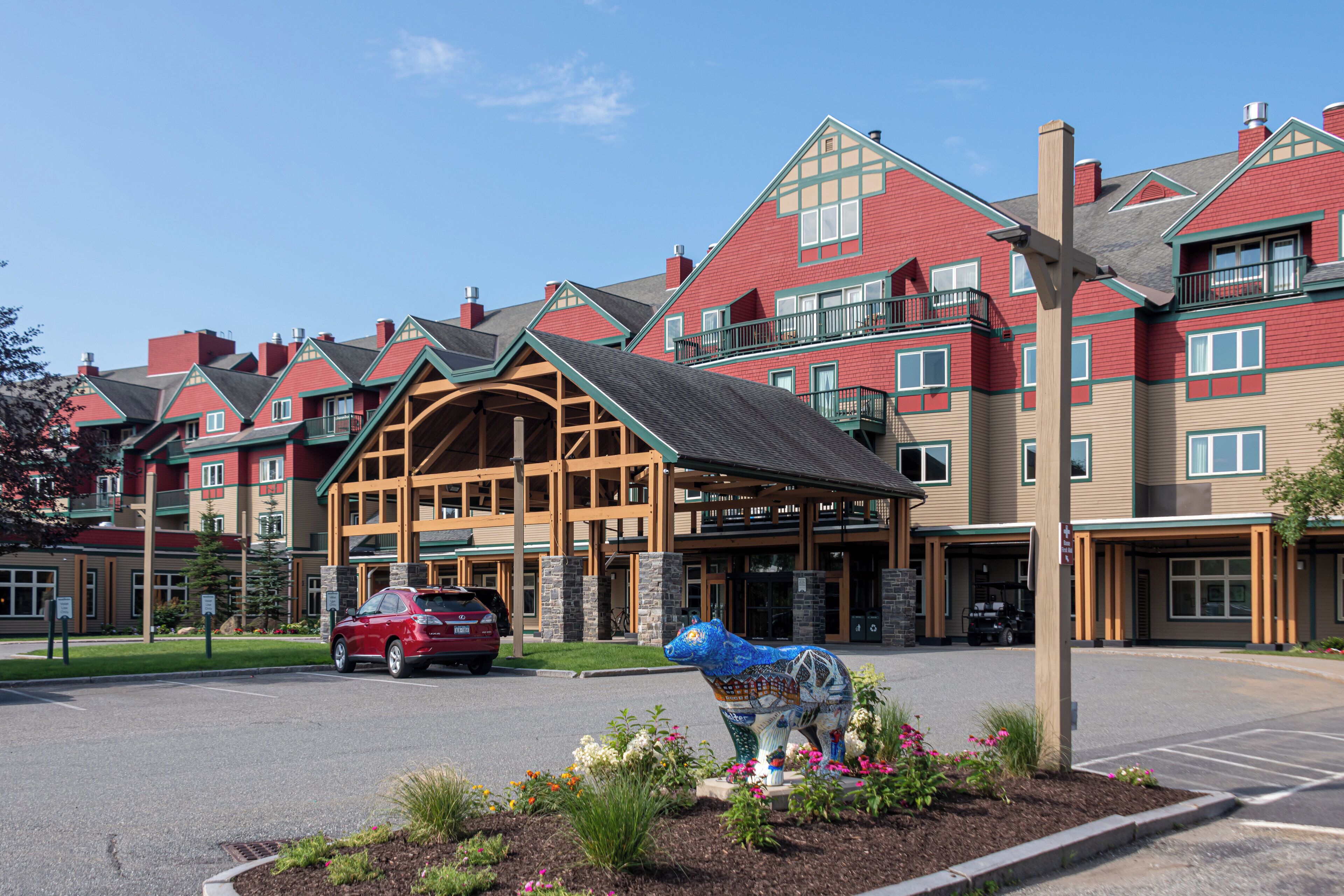 A multi-story hotel with a prominent entrance, a parking area, and a decorative bear statue.