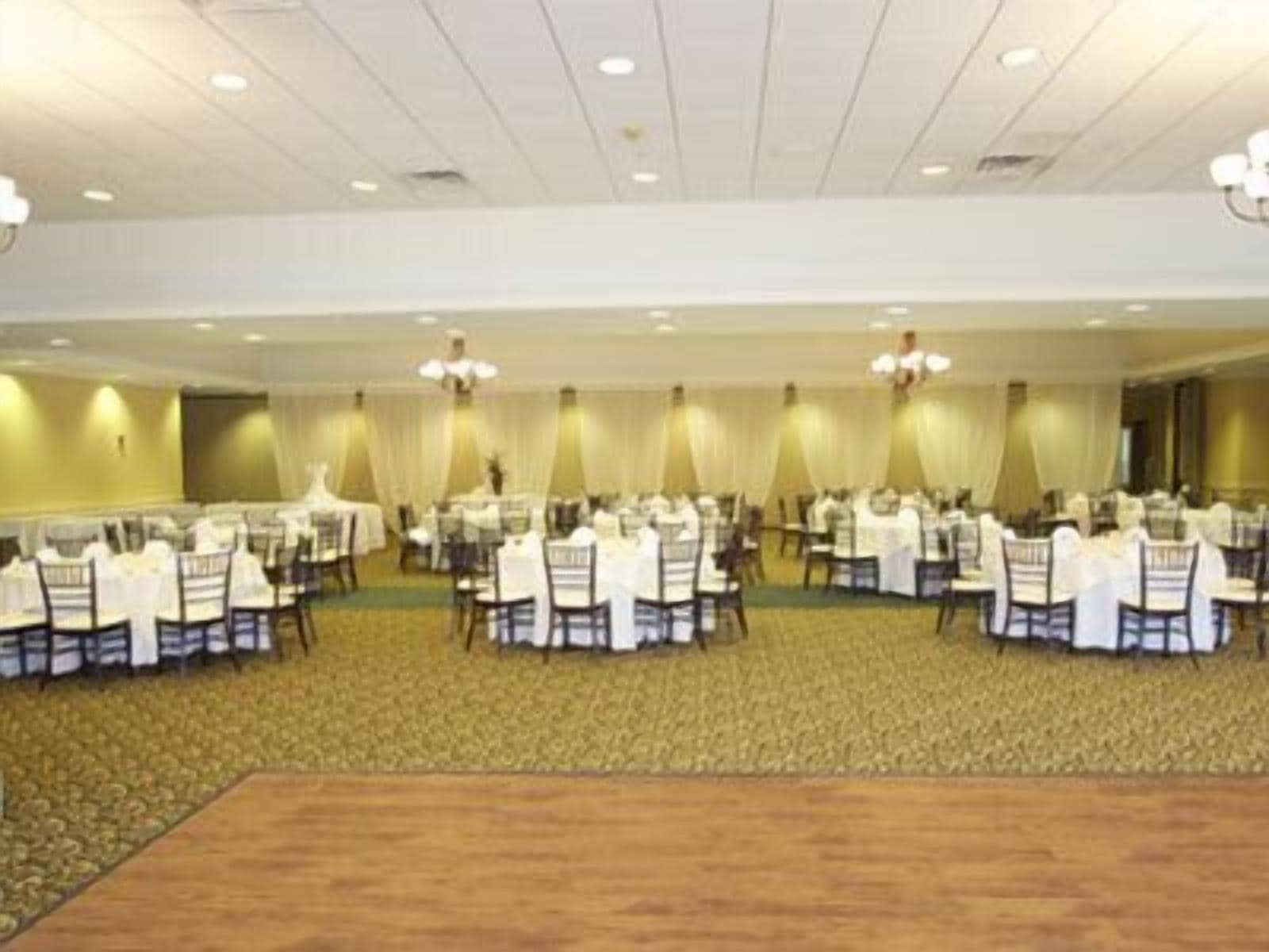 Un salón de banquetes con mesas redondas y sillas, suelo alfombrado y candelabros.