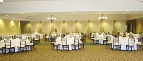 A banquet hall with round tables and chairs, carpeted flooring, and chandeliers.