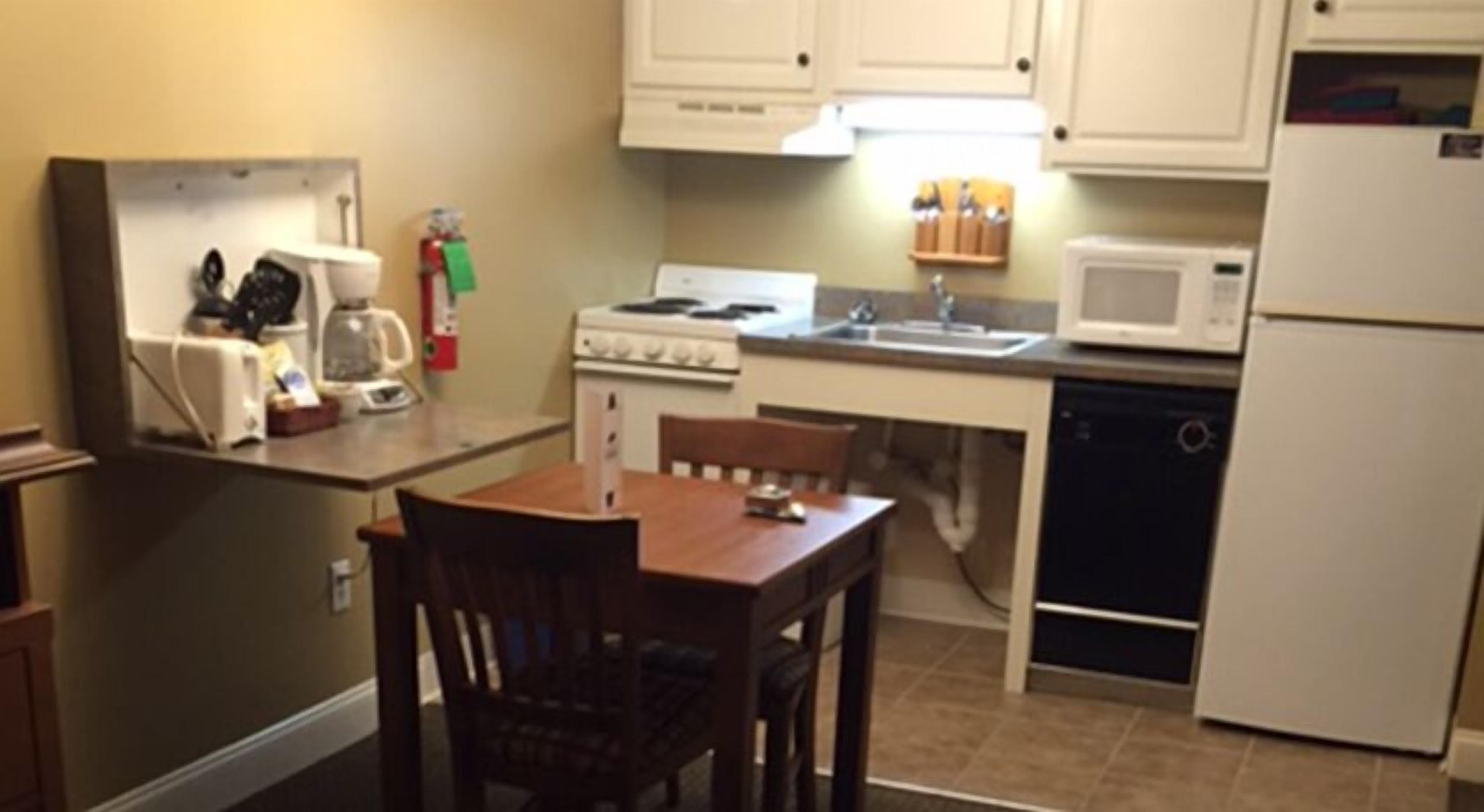 Une cuisine compacte équipée d’une cuisinière, d’un four à micro-ondes, d’un évier et d’une petite table à manger avec des chaises.